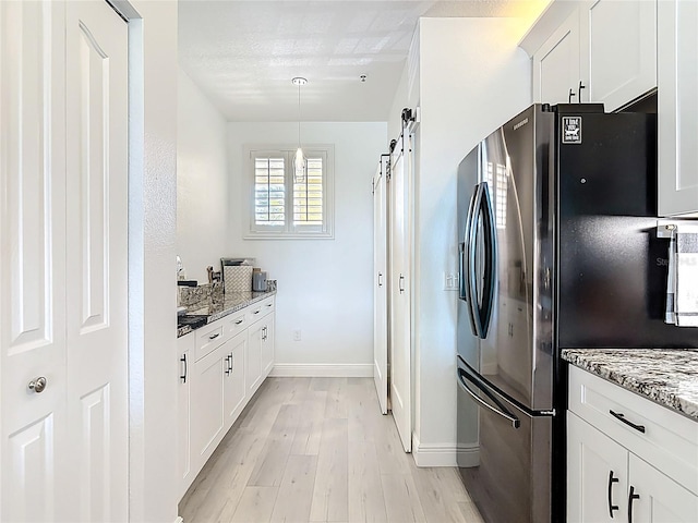 kitchen with a barn door, light wood-style flooring, light stone counters, and freestanding refrigerator