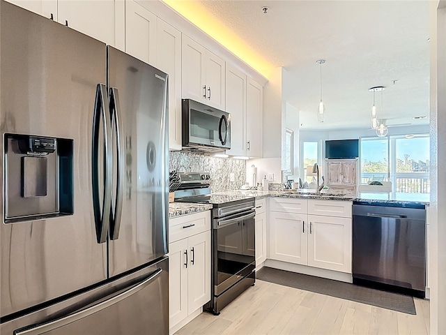 kitchen featuring light stone countertops, decorative backsplash, appliances with stainless steel finishes, white cabinetry, and a sink