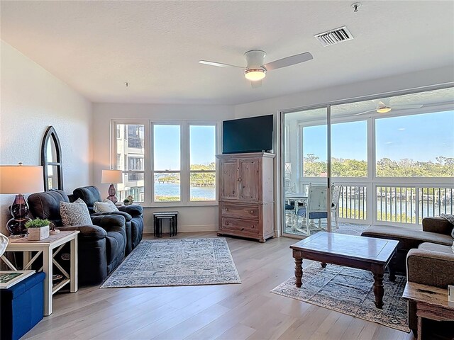 living room with a ceiling fan, light wood-style floors, visible vents, and a healthy amount of sunlight