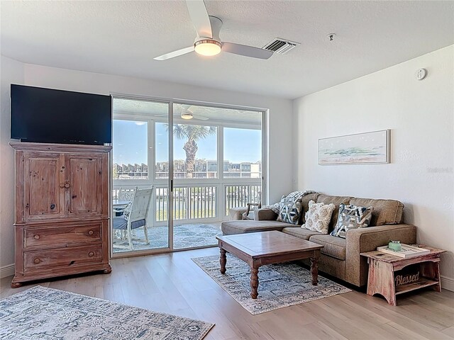 living room featuring visible vents, a textured ceiling, ceiling fan, and light wood finished floors