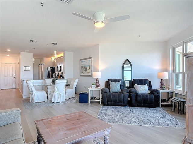 living room with visible vents, baseboards, light wood-style flooring, and a ceiling fan