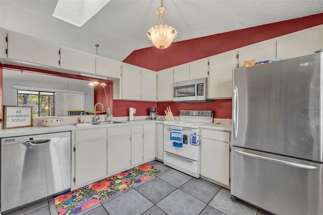 kitchen featuring light tile patterned floors, light countertops, appliances with stainless steel finishes, a sink, and vaulted ceiling with skylight