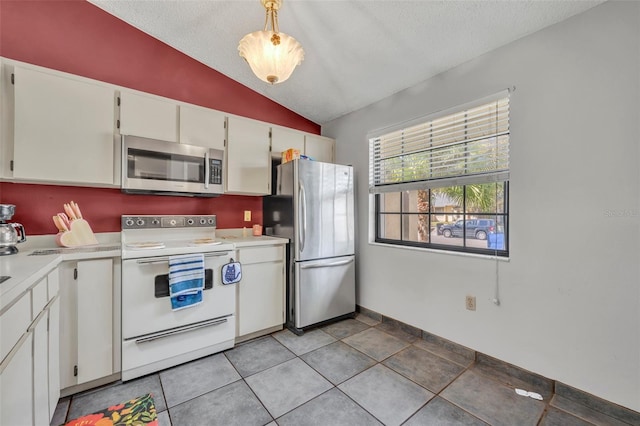 kitchen with light tile patterned floors, stainless steel appliances, light countertops, white cabinets, and vaulted ceiling