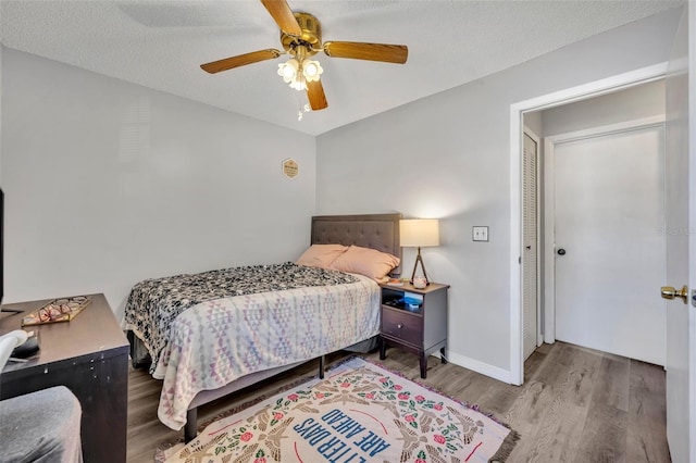 bedroom with a ceiling fan, a textured ceiling, baseboards, and wood finished floors