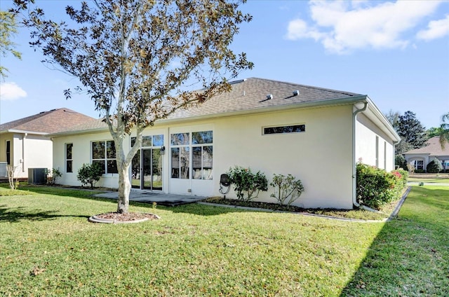 rear view of property featuring central air condition unit, stucco siding, a lawn, and roof with shingles