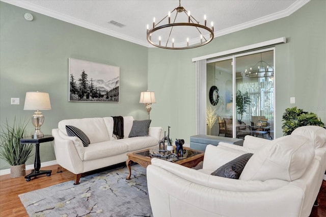 living room with visible vents, wood finished floors, crown molding, baseboards, and a chandelier