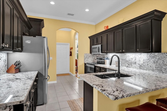 kitchen with a sink, arched walkways, appliances with stainless steel finishes, light tile patterned floors, and light stone countertops