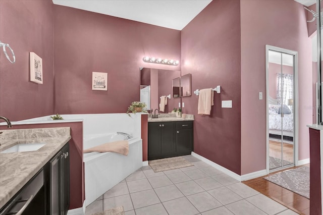 ensuite bathroom with a sink, a garden tub, two vanities, and tile patterned flooring