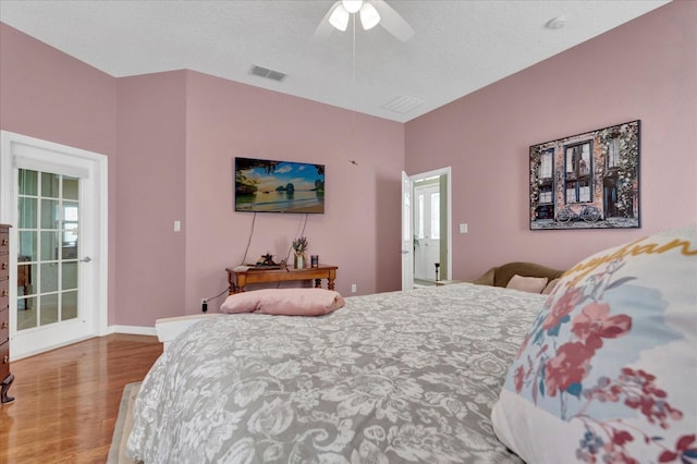 bedroom with visible vents, a textured ceiling, wood finished floors, baseboards, and ceiling fan