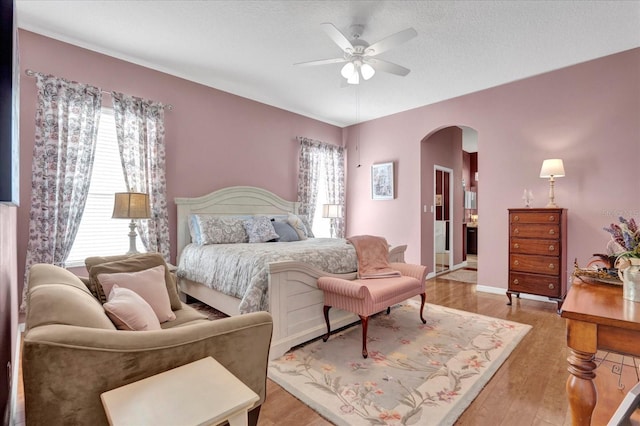 bedroom with arched walkways, light wood finished floors, a textured ceiling, and a ceiling fan