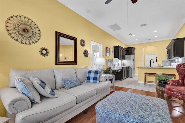 living room with arched walkways, visible vents, crown molding, and a ceiling fan