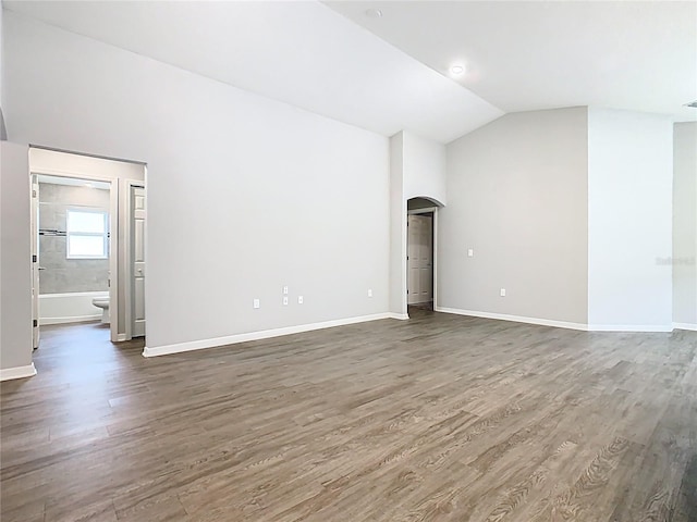 unfurnished living room with arched walkways, wood finished floors, baseboards, and vaulted ceiling