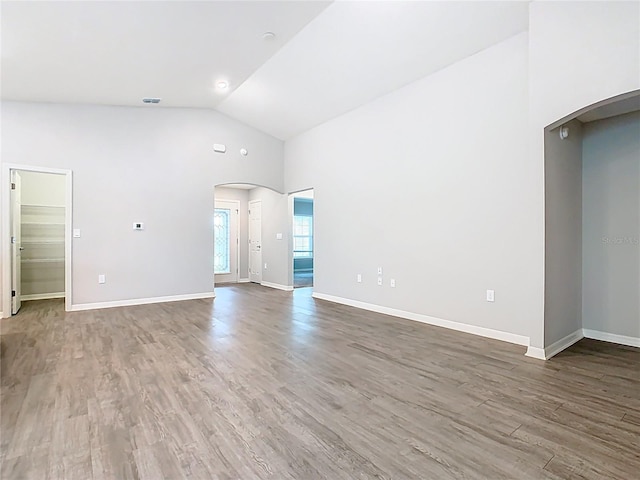 unfurnished living room featuring arched walkways, baseboards, and wood finished floors