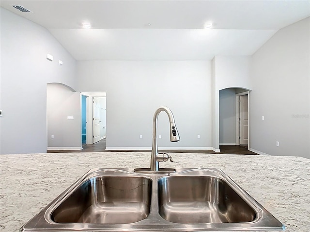 kitchen with arched walkways, visible vents, lofted ceiling, and a sink