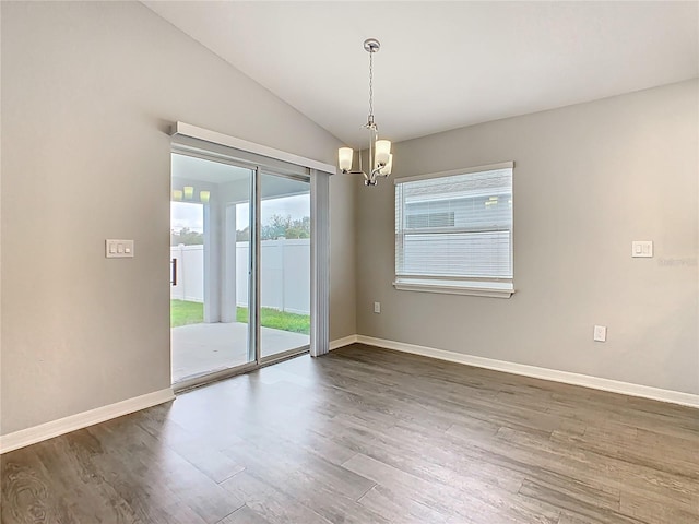 spare room featuring a notable chandelier, vaulted ceiling, baseboards, and wood finished floors