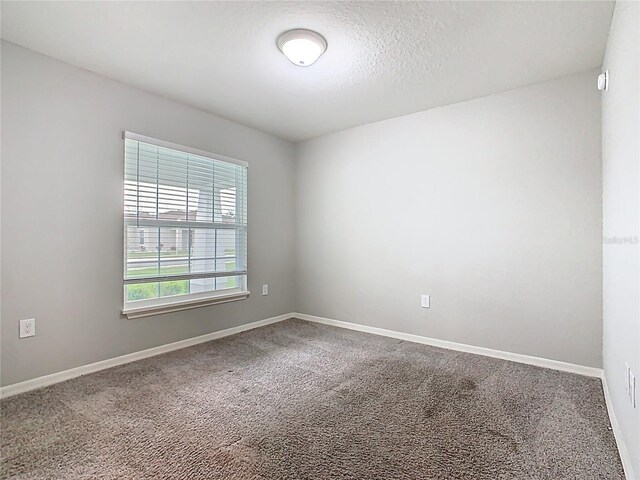 empty room with carpet flooring, a textured ceiling, and baseboards