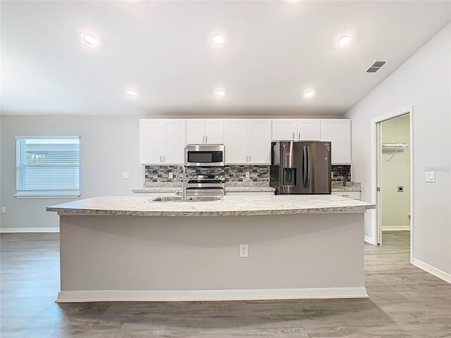 kitchen with a center island with sink, visible vents, a sink, stainless steel appliances, and white cabinets