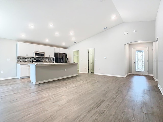 kitchen with an island with sink, lofted ceiling, decorative backsplash, appliances with stainless steel finishes, and white cabinets