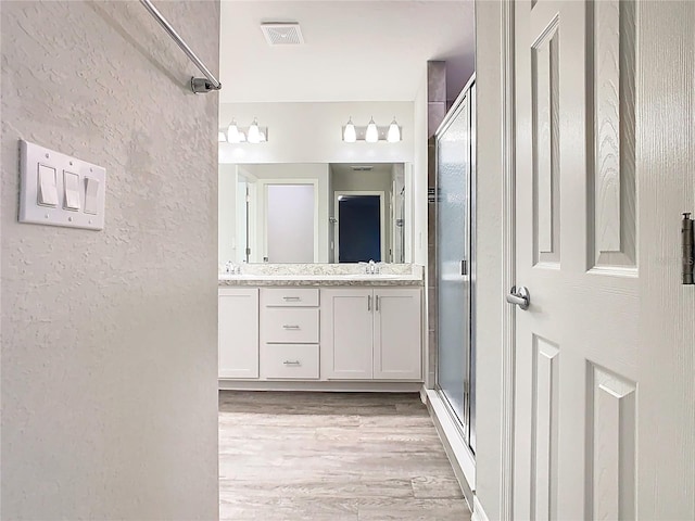 full bathroom featuring wood finished floors, visible vents, double vanity, a stall shower, and a sink