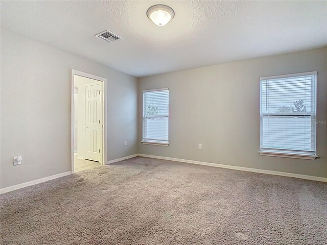 empty room featuring visible vents, baseboards, light colored carpet, and a textured ceiling