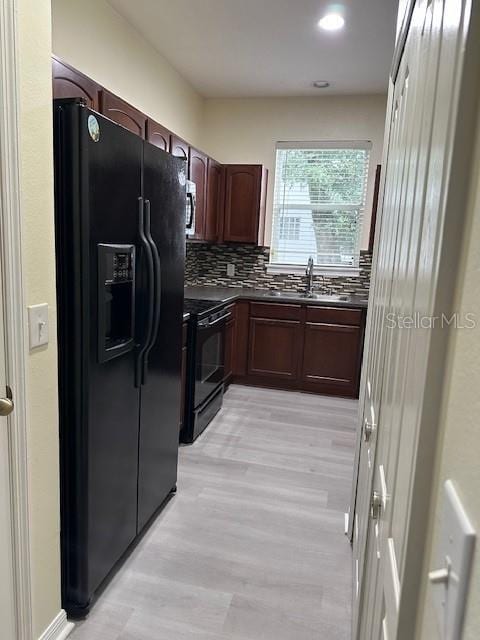 kitchen featuring light wood finished floors, decorative backsplash, dark countertops, black appliances, and a sink