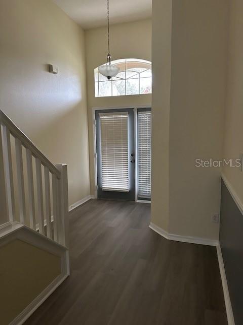 entryway featuring stairs, dark wood-style flooring, a towering ceiling, and baseboards