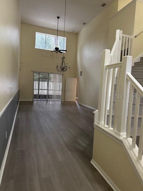 unfurnished dining area with stairway, a towering ceiling, baseboards, and wood finished floors