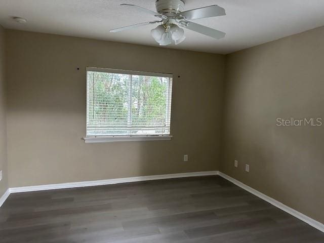 spare room featuring baseboards, dark wood finished floors, and a ceiling fan