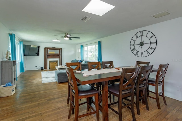 dining space featuring a ceiling fan, visible vents, wood-type flooring, and a tile fireplace