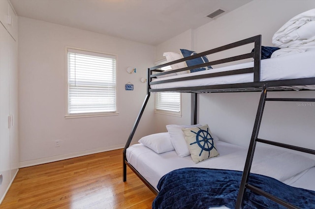 bedroom featuring visible vents, multiple windows, baseboards, and wood finished floors