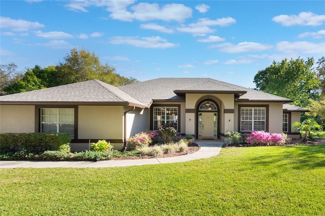 ranch-style house with stucco siding, a shingled roof, and a front yard