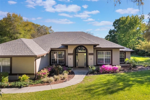 ranch-style home with a shingled roof, a front lawn, and stucco siding