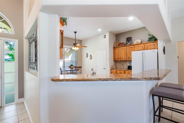 kitchen with visible vents, a breakfast bar, backsplash, freestanding refrigerator, and light tile patterned floors