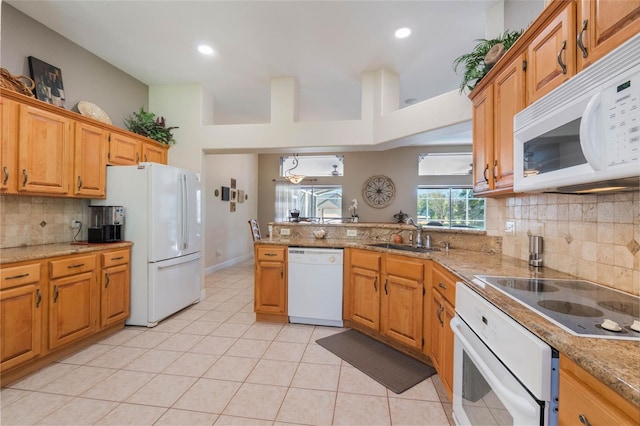 kitchen featuring white appliances, light tile patterned floors, light stone countertops, a peninsula, and a sink