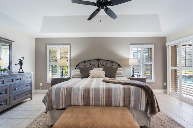 bedroom featuring light tile patterned floors, a tray ceiling, baseboards, and ceiling fan