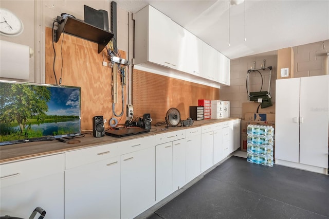 kitchen featuring light countertops, finished concrete floors, concrete block wall, and white cabinetry