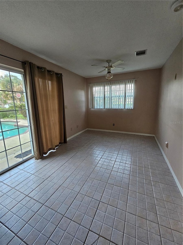 empty room featuring a textured ceiling, light tile patterned floors, visible vents, and ceiling fan