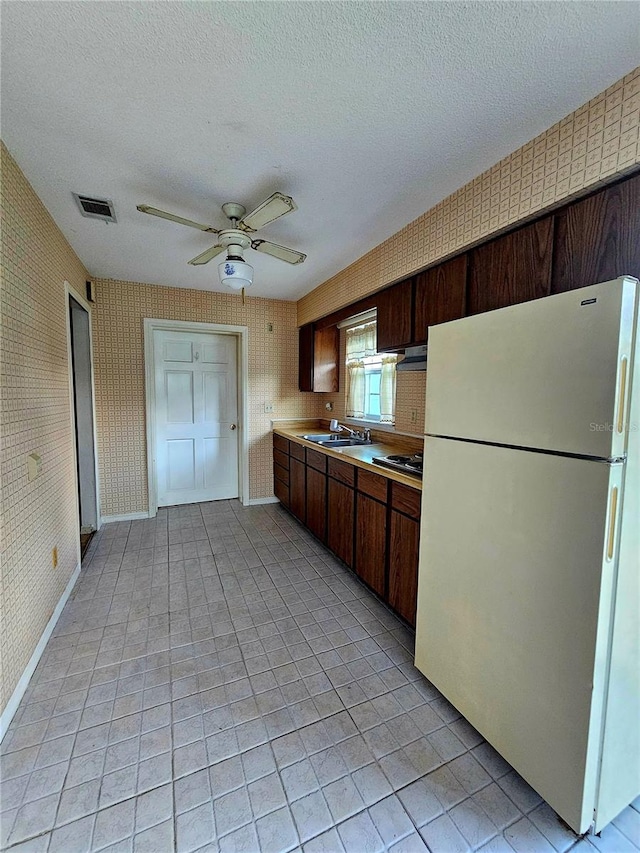 kitchen with visible vents, a textured ceiling, freestanding refrigerator, wallpapered walls, and light countertops