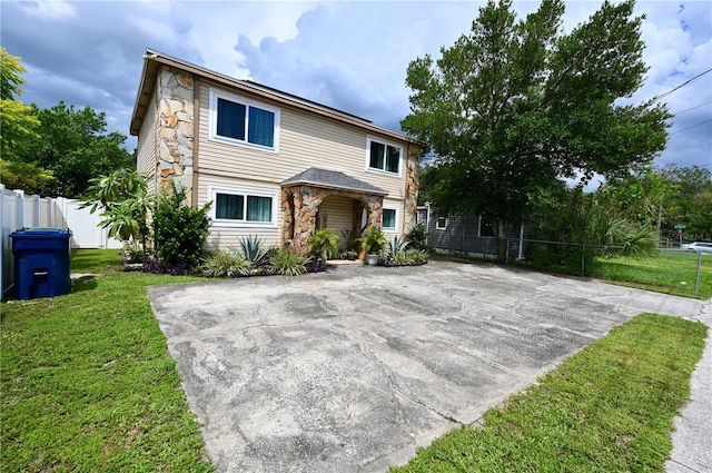 view of front of house with stone siding, a front yard, and fence