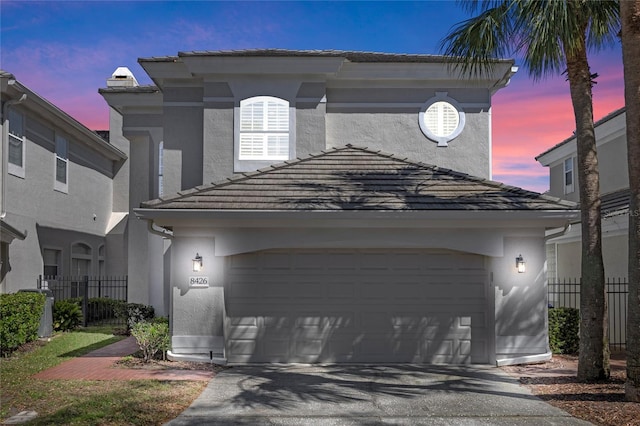 view of front of home with an attached garage, a tile roof, fence, and stucco siding