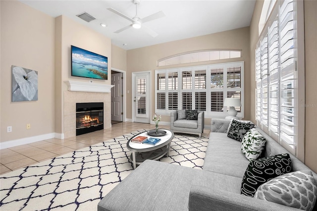 tiled living room featuring a ceiling fan, a tile fireplace, visible vents, and baseboards