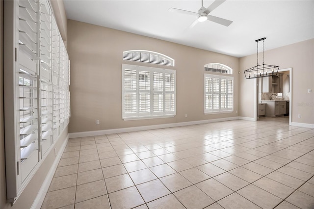 empty room with ceiling fan with notable chandelier, light tile patterned flooring, a sink, and baseboards