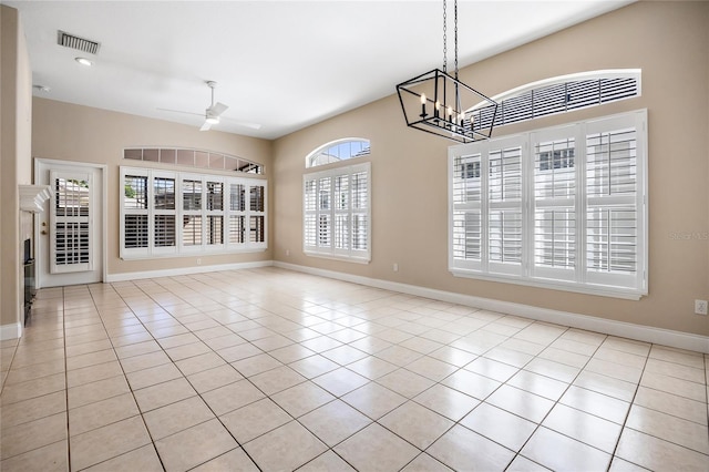 tiled spare room with baseboards, visible vents, and ceiling fan with notable chandelier