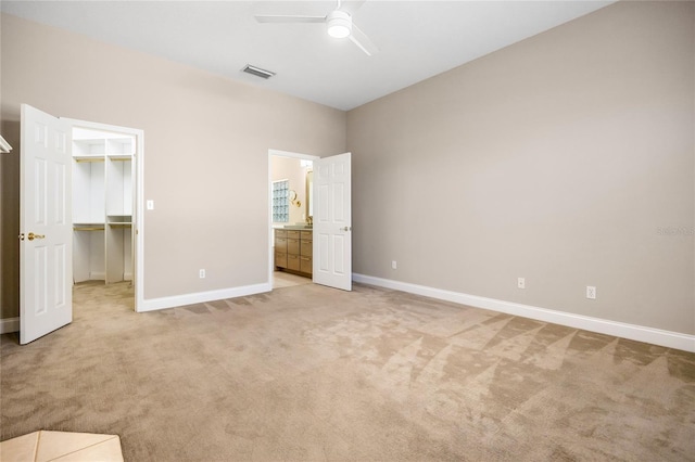 unfurnished bedroom with light colored carpet, visible vents, baseboards, a spacious closet, and ensuite bath