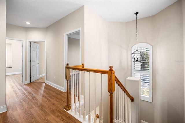 hall with a chandelier, wood finished floors, an upstairs landing, and baseboards