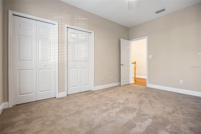 unfurnished bedroom with carpet floors, multiple closets, visible vents, ceiling fan, and baseboards