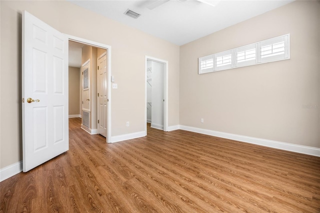 unfurnished bedroom featuring wood finished floors, visible vents, baseboards, a closet, and a walk in closet