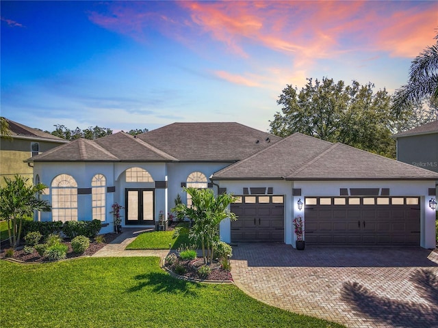 view of front of home featuring an attached garage, stucco siding, decorative driveway, and a front yard