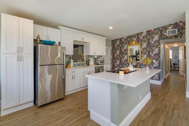 kitchen featuring visible vents, wallpapered walls, freestanding refrigerator, a sink, and white cabinets