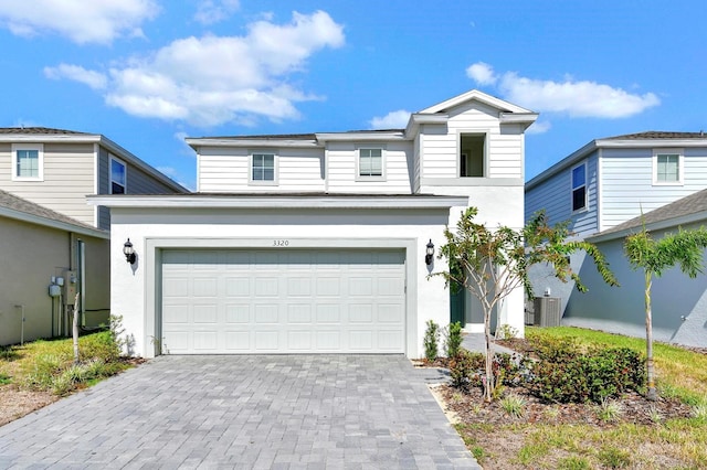 traditional-style home with an attached garage, central AC, decorative driveway, and stucco siding